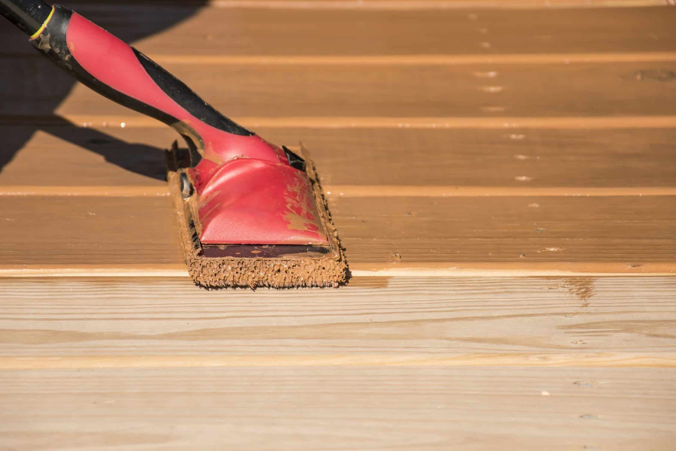 Staining a wooden deck with a staining pad.